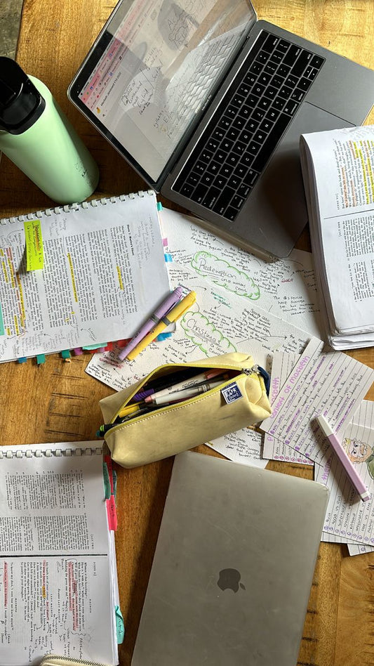 Ein aufgeschlagener Laptop liegt auf einem Holztisch, umgeben von handschriftlichen Notizen, Lernkarten, farblich markierten Skripten und einem Federmäppchen mit Markern. Perfektes Setup für produktives Lernen und effiziente Studienorganisation.