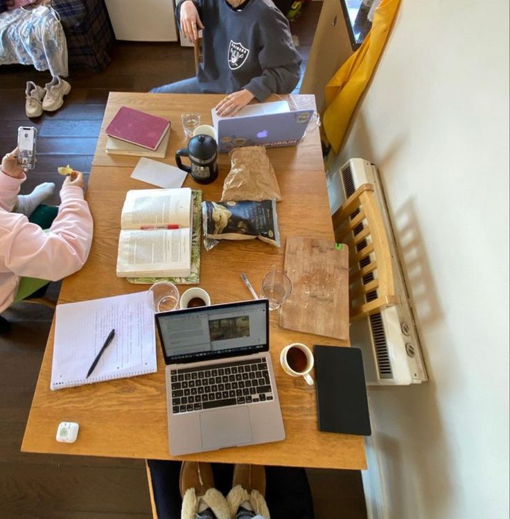 Ein gemeinsamer Lernplatz mit Laptops, Notizbüchern, Lehrbüchern und Kaffee auf einem Holztisch – die perfekte Uni Essentials Checklist (Deutsch) für produktives Studieren in einer WG oder Lerngruppe.